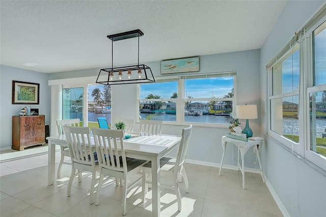 tiled dining space with a textured ceiling, a water view, and plenty of natural light