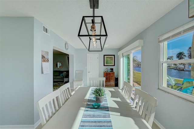 dining space featuring a chandelier, a textured ceiling, a water view, and a healthy amount of sunlight