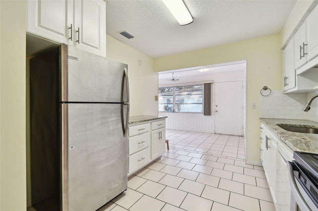 kitchen with stainless steel appliances, sink, white cabinets, light stone counters, and a textured ceiling