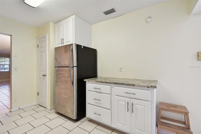 kitchen with a textured ceiling, stainless steel fridge, white cabinetry, light stone counters, and light tile patterned floors