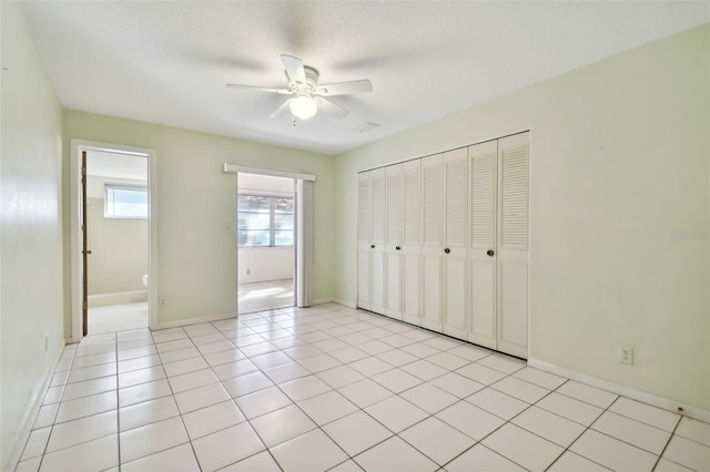 unfurnished bedroom featuring a closet, a textured ceiling, light tile patterned flooring, and ceiling fan