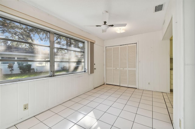 unfurnished bedroom featuring a closet, wooden walls, light tile patterned floors, and ceiling fan