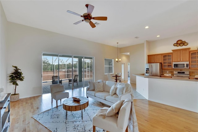 living room featuring ceiling fan with notable chandelier and light wood-type flooring