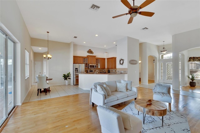 living room with sink, decorative columns, ceiling fan with notable chandelier, and light wood-type flooring