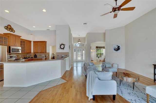 kitchen with decorative backsplash, stainless steel appliances, light wood-type flooring, and ceiling fan