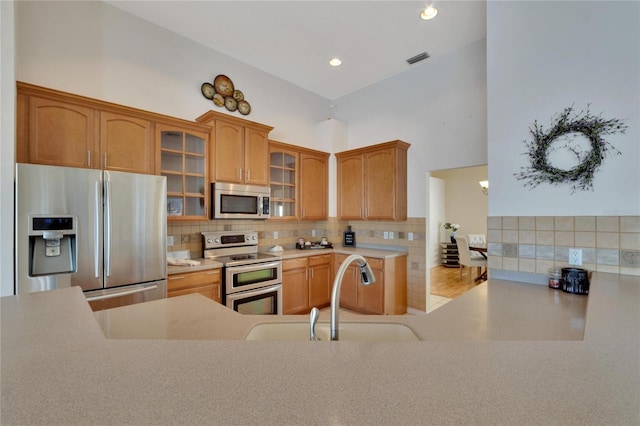 kitchen with a high ceiling, stainless steel appliances, sink, light hardwood / wood-style floors, and tasteful backsplash