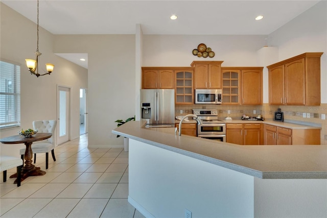 kitchen with decorative backsplash, pendant lighting, light tile patterned floors, a chandelier, and appliances with stainless steel finishes