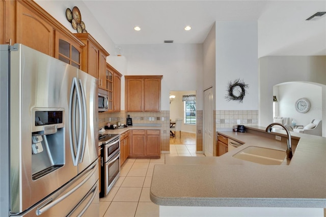 kitchen featuring kitchen peninsula, tasteful backsplash, light tile patterned flooring, sink, and stainless steel appliances