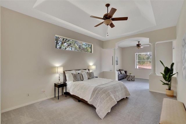 carpeted bedroom with decorative columns, a raised ceiling, and ceiling fan