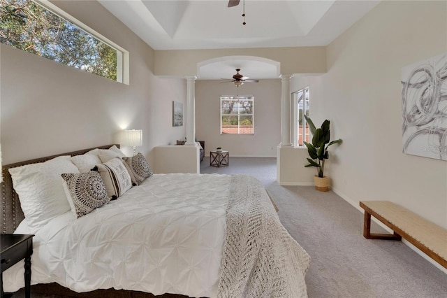 bedroom featuring a raised ceiling, ceiling fan, carpet, and decorative columns