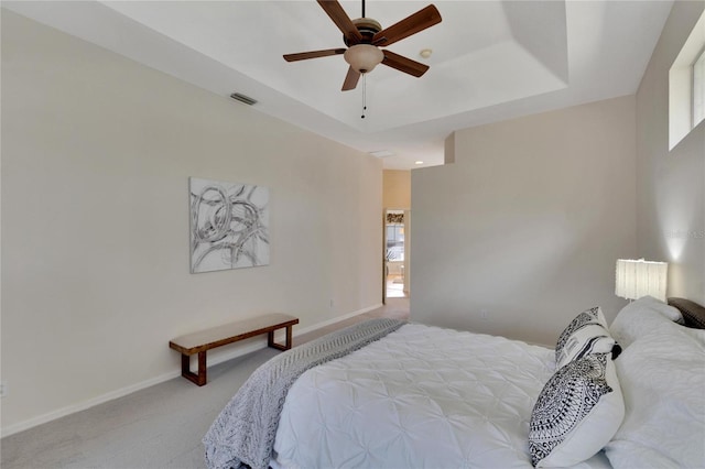 bedroom with a tray ceiling, multiple windows, light colored carpet, and ceiling fan