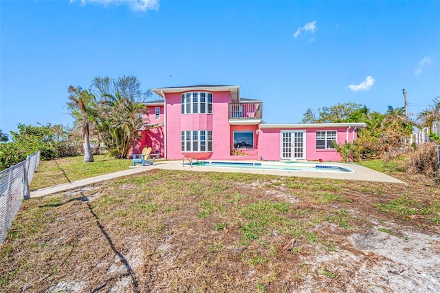 back of property featuring a yard, french doors, a balcony, a fenced in pool, and a patio area