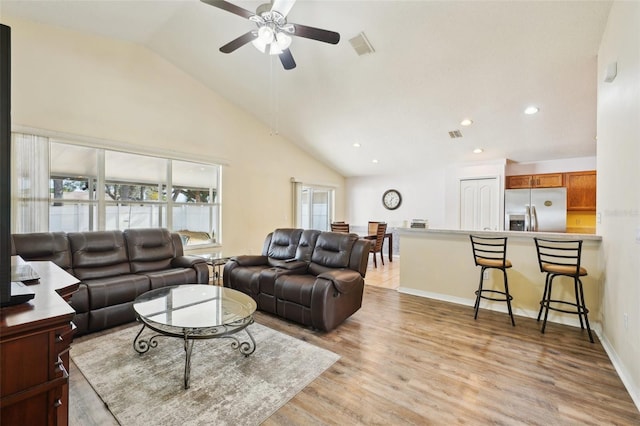 living room with ceiling fan, vaulted ceiling, and light wood-type flooring