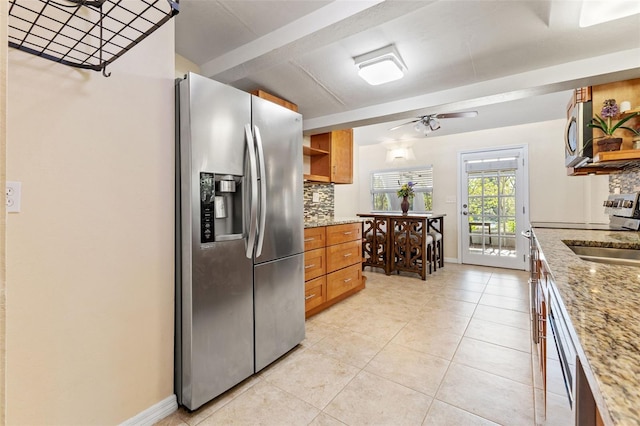 kitchen featuring backsplash, light tile patterned floors, appliances with stainless steel finishes, light stone counters, and ceiling fan