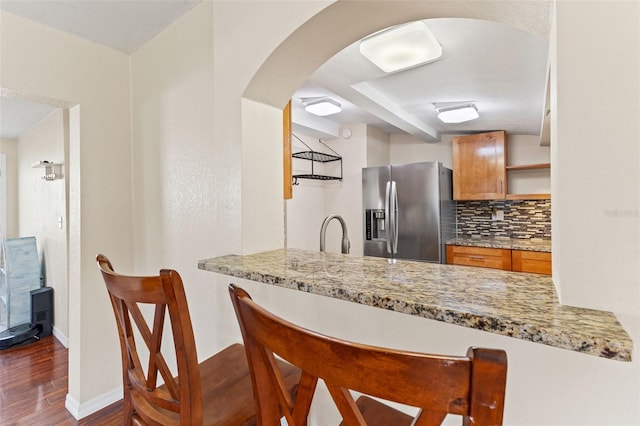 kitchen with decorative backsplash, stainless steel fridge, light stone counters, and dark wood-type flooring