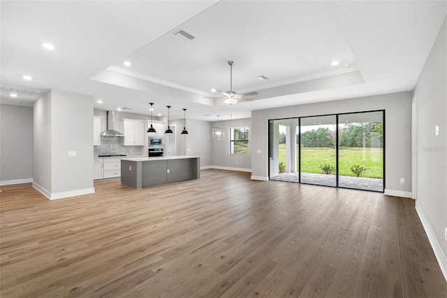 unfurnished living room featuring crown molding, ceiling fan, hardwood / wood-style flooring, and a raised ceiling