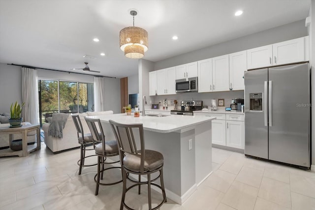 kitchen featuring appliances with stainless steel finishes, sink, hanging light fixtures, white cabinets, and a center island with sink