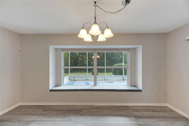 unfurnished room featuring a textured ceiling, hardwood / wood-style flooring, and a chandelier