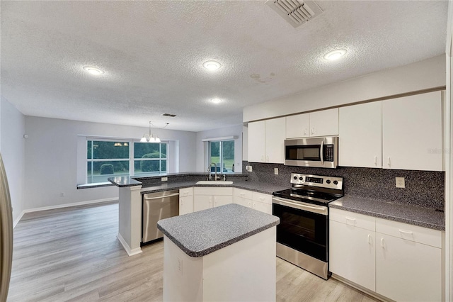 kitchen featuring white cabinets, a kitchen island, appliances with stainless steel finishes, a textured ceiling, and light hardwood / wood-style floors