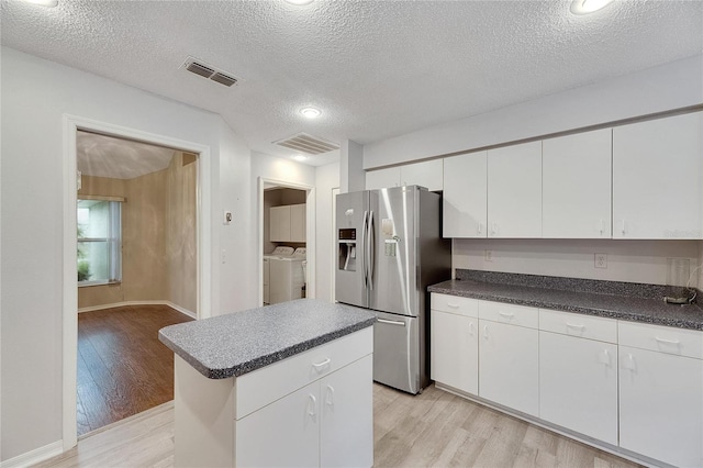 kitchen with white cabinets, a textured ceiling, light wood-type flooring, and stainless steel fridge