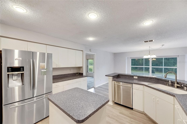 kitchen featuring stainless steel appliances, sink, a center island, white cabinetry, and a textured ceiling