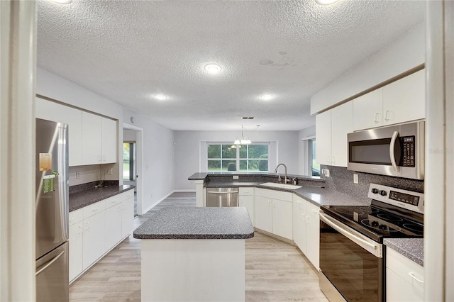 kitchen with a kitchen island, sink, light wood-type flooring, white cabinetry, and appliances with stainless steel finishes