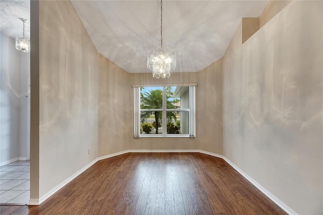 spare room with a textured ceiling, vaulted ceiling, a notable chandelier, and wood-type flooring