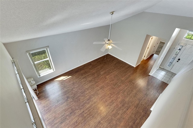 unfurnished living room featuring dark wood-type flooring, a textured ceiling, high vaulted ceiling, and ceiling fan