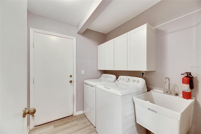 laundry room featuring sink, light wood-type flooring, independent washer and dryer, a textured ceiling, and cabinets