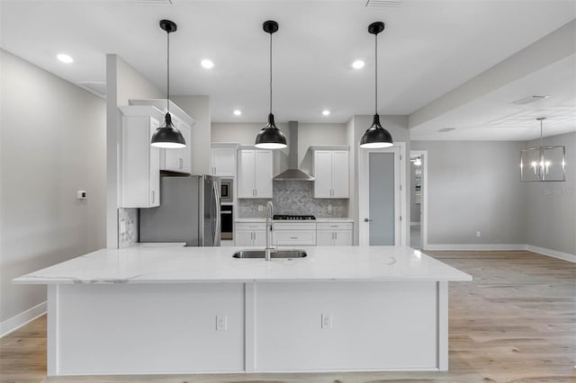 kitchen with wall chimney range hood, sink, appliances with stainless steel finishes, hanging light fixtures, and white cabinetry