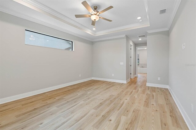 unfurnished room with ornamental molding, ceiling fan, light wood-type flooring, and a raised ceiling