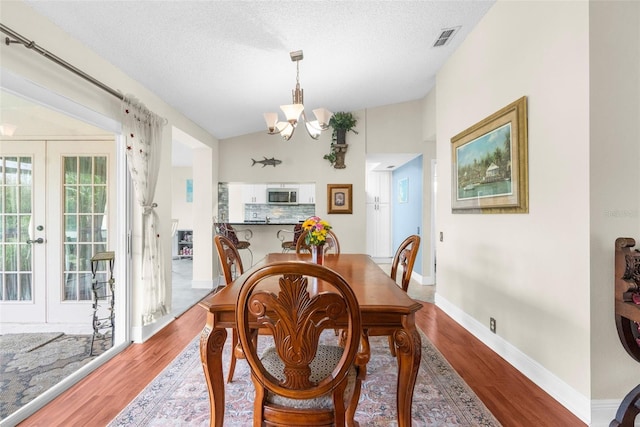 dining area featuring lofted ceiling, hardwood / wood-style floors, a textured ceiling, and a chandelier