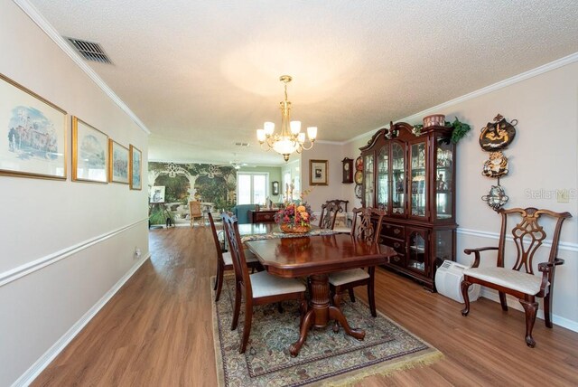 dining area featuring ornamental molding, hardwood / wood-style floors, a textured ceiling, and an inviting chandelier