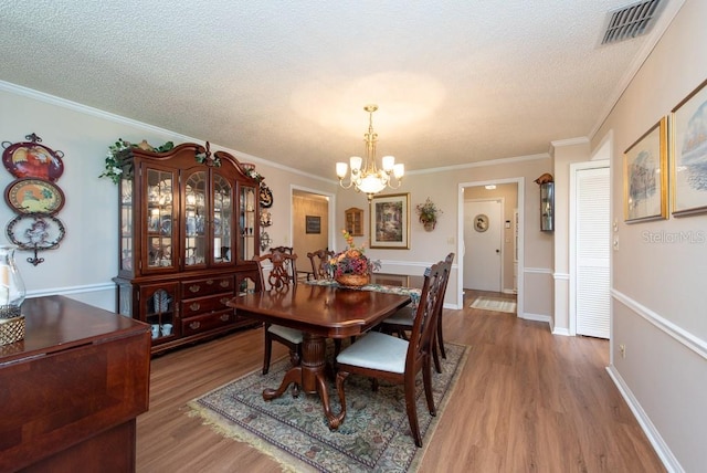 dining room featuring ornamental molding, a textured ceiling, a notable chandelier, and wood-type flooring