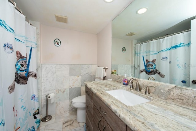 bathroom with toilet, vanity, and tile walls