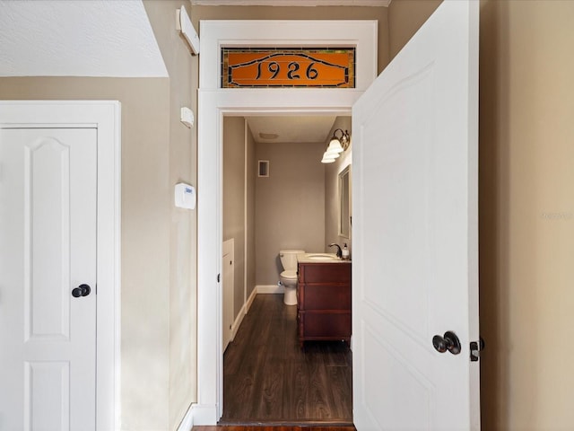 hallway featuring dark wood-style floors, visible vents, a sink, and baseboards