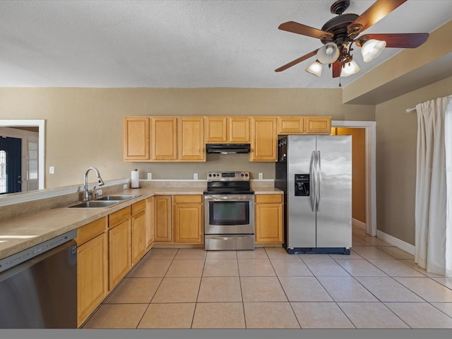 kitchen featuring light tile patterned floors, stainless steel appliances, light brown cabinets, a sink, and under cabinet range hood