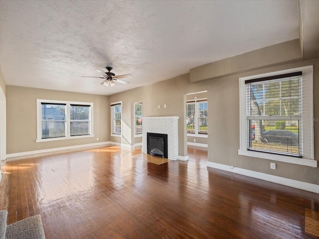 unfurnished living room with ceiling fan, a fireplace, a healthy amount of sunlight, and wood-type flooring