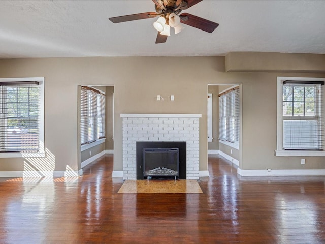 unfurnished living room featuring a brick fireplace, a healthy amount of sunlight, baseboards, and wood finished floors