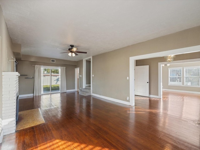 unfurnished living room with a brick fireplace, wood-type flooring, and ceiling fan with notable chandelier