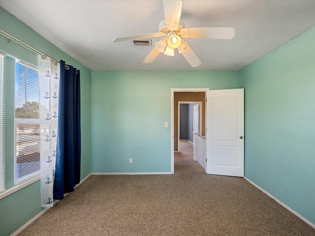 empty room featuring a ceiling fan, carpet flooring, visible vents, and baseboards