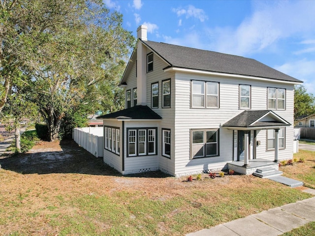 view of front of house with roof with shingles, a chimney, a front yard, and fence