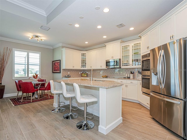 kitchen with a center island with sink, light stone counters, appliances with stainless steel finishes, light hardwood / wood-style floors, and sink