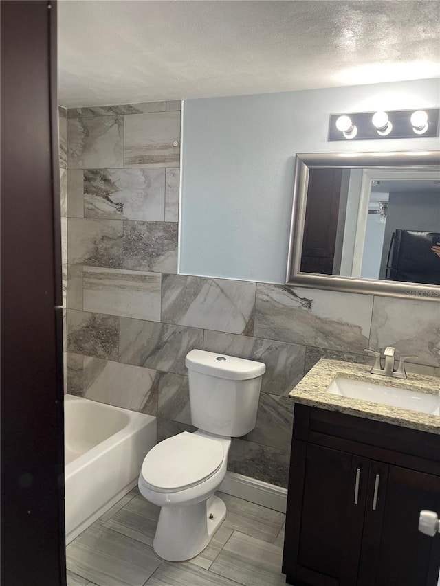 bathroom featuring vanity, toilet, tile walls, and a textured ceiling