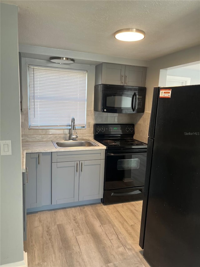 kitchen featuring black appliances, sink, light wood-type flooring, and gray cabinets