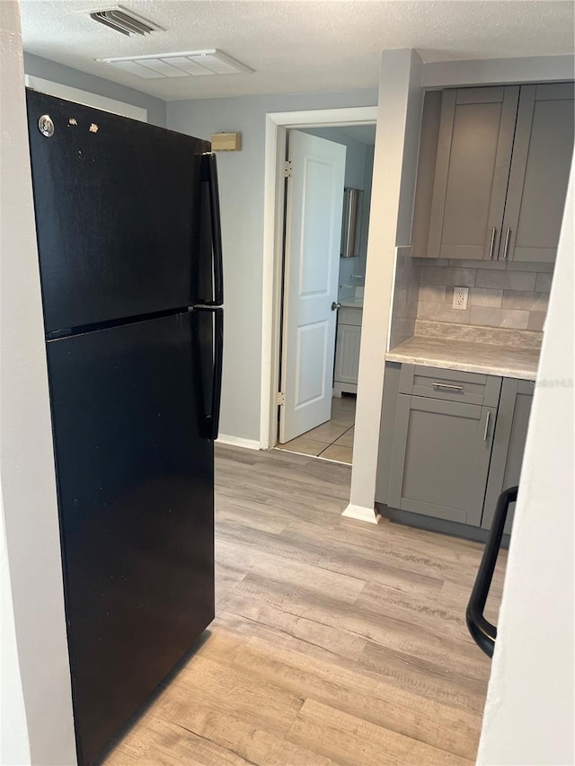 kitchen with black fridge, gray cabinets, a textured ceiling, light hardwood / wood-style floors, and tasteful backsplash