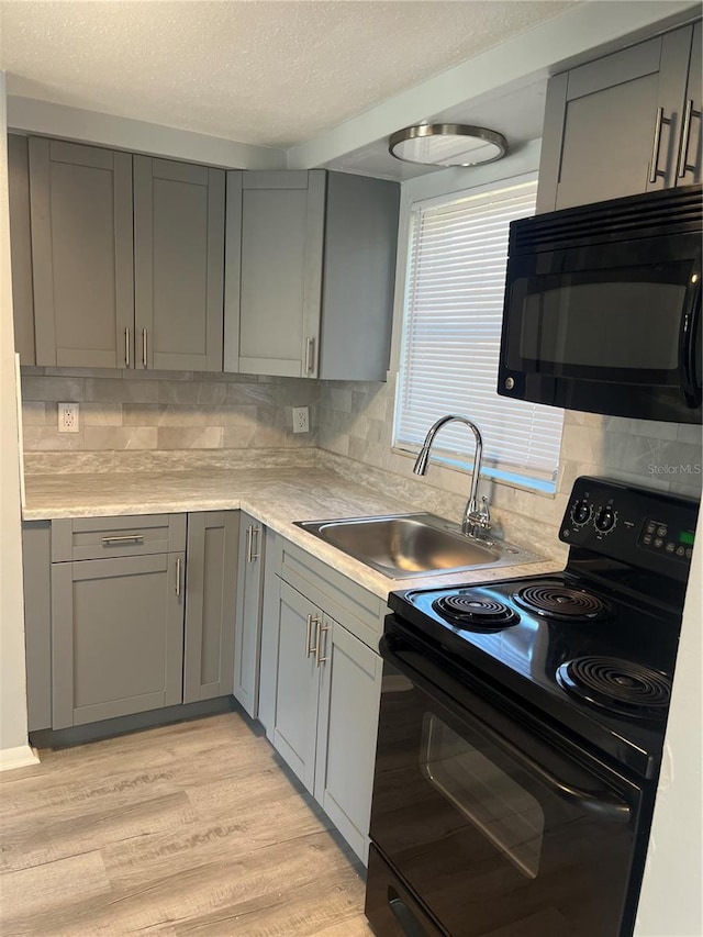 kitchen with decorative backsplash, gray cabinetry, sink, black appliances, and light hardwood / wood-style floors