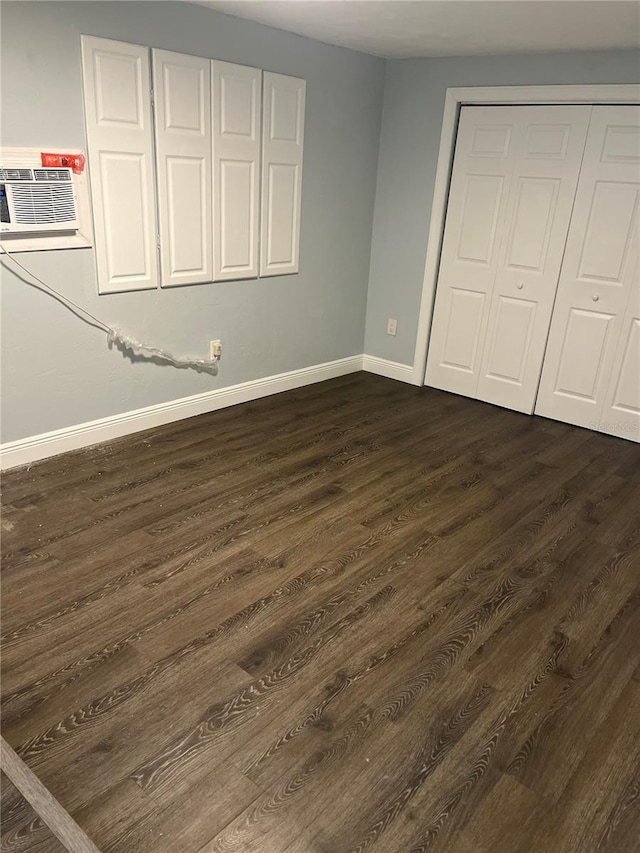 unfurnished bedroom featuring an AC wall unit, a closet, and dark hardwood / wood-style flooring