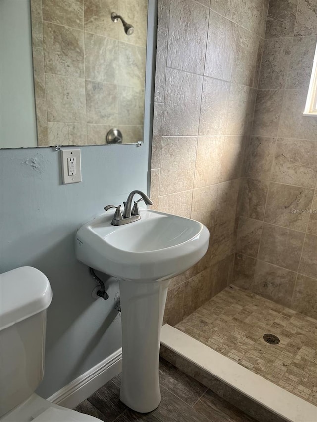 bathroom with toilet, sink, tiled shower, and hardwood / wood-style floors