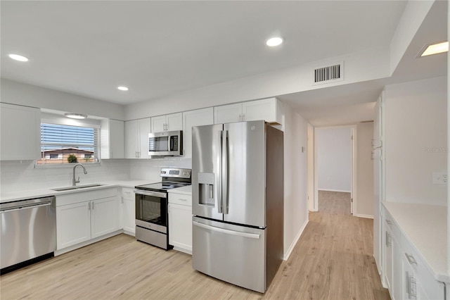 kitchen with white cabinets, tasteful backsplash, appliances with stainless steel finishes, light wood-type flooring, and sink